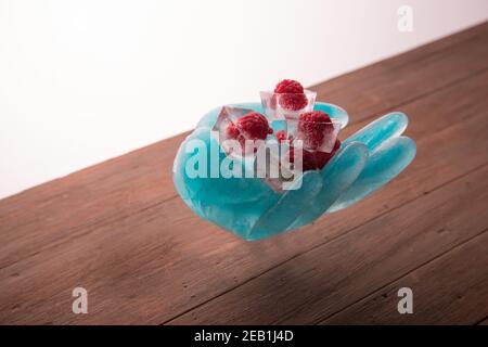 Une sculpture sur glace en forme de main tient framboises congelées en cubes de glace Banque D'Images