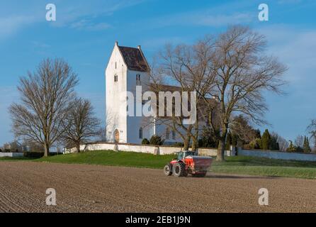 Kalveavoir Danemark - avril 17. 2018 : agriculteur sur un tracteur massey Ferguson, qui étale de l'engrais avec l'église de Kalveheont en arrière-plan Banque D'Images