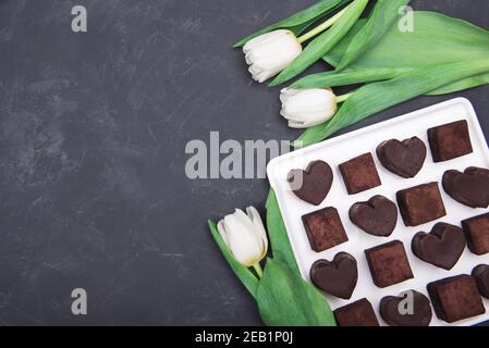 Présenter une boîte de bonbons au chocolat coeurs et tulipes sur fond sombre. Désert pour la Saint-Valentin Banque D'Images