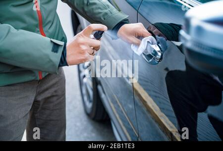 La main de l'homme vaporise un spray désinfectant sur la poignée de la porte de la voiture, essuyer les surfaces qui sont fréquemment touchées Banque D'Images