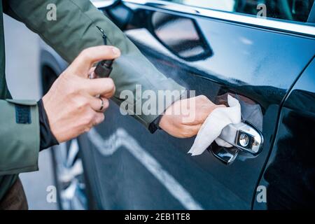 La main de l'homme vaporise un spray désinfectant sur la poignée de la porte de la voiture, essuyer les surfaces qui sont fréquemment touchées Banque D'Images