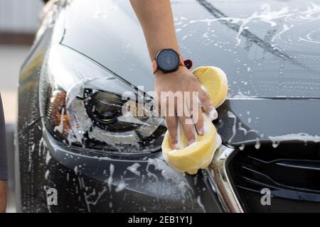 Laver la voiture à la main à l'eau savonneuse. L'homme nettoie la voiture avec une éponge, de l'eau et du détergent. Banque D'Images