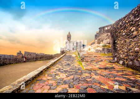 Arc-en-ciel sur Portovenere (Porto Venere) en Ligurie, Italie: Vue panoramique de l'église Saint-Pierre (Chiesa di San Pietro) au coucher du soleil avec coucher de soleil coloré Banque D'Images