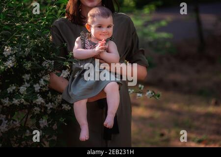 Portrait en gros plan d'un bébé heureux qui se claque les mains dans les bras d'une belle mère. Une jeune femme marche avec sa fille dans un parc vert près de TH Banque D'Images