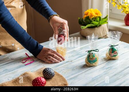 Femme empaquante des œufs de pâques comme cadeau pour la fête de Pâques. Faire et emballer la décoration maison sur la table Banque D'Images