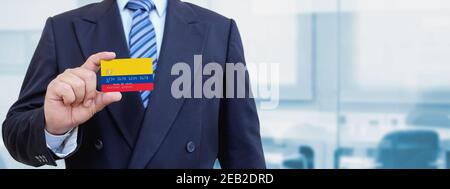 Image rognée d'un homme d'affaires tenant une carte de crédit en plastique avec drapeau imprimé de la Colombie. Arrière-plan flou. Banque D'Images