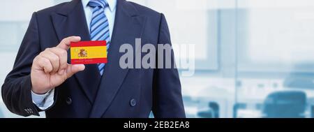 Image rognée d'un homme d'affaires tenant une carte de crédit en plastique avec drapeau imprimé de l'Espagne. Arrière-plan flou. Banque D'Images