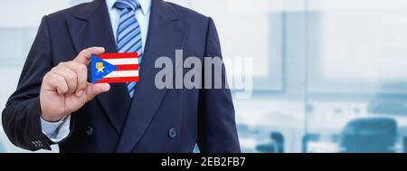 Image rognée d'un homme d'affaires tenant une carte de crédit en plastique avec drapeau imprimé de Porto Rico. Arrière-plan flou. Banque D'Images