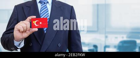 Image rognée d'un homme d'affaires tenant une carte de crédit en plastique avec drapeau imprimé de Turquie. Arrière-plan flou. Banque D'Images