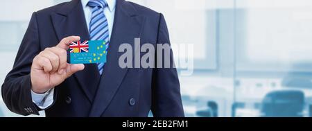 Image rognée d'un homme d'affaires tenant une carte de crédit en plastique avec drapeau imprimé de Tuvalu. Arrière-plan flou. Banque D'Images