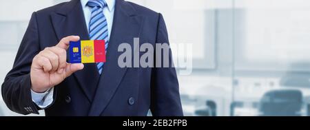 Image rognée d'un homme d'affaires tenant une carte de crédit en plastique avec drapeau imprimé d'Andorre. Arrière-plan flou. Banque D'Images