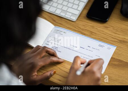 Une femme africaine signant un chèque de banque ou un chèque de paie Banque D'Images