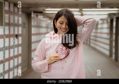 Jeune femme magnifique tenant les coeurs à la main, portant un pull à capuche rose. Joyeux, expressions amusantes, portrait de gros plan. Concept de la Saint-Valentin Banque D'Images