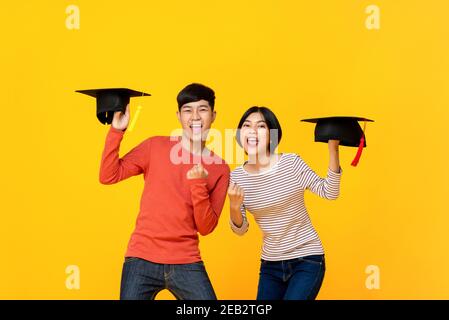 Des étudiants asiatiques enthousiastes et heureux avec des casquettes hautes en couleur fond de studio jaune Banque D'Images