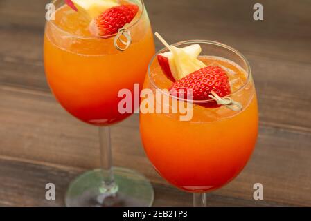 Boissons rafraîchissantes aux verres pour un cocktail de lever de soleil à l'orange et à la fraise sur fond de table en bois Banque D'Images