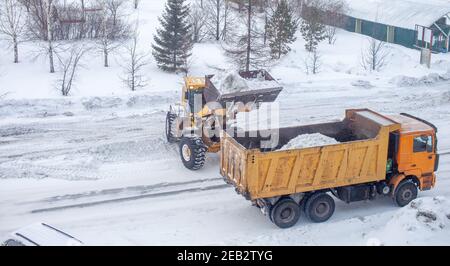 Le gros tracteur jaune nettoie la neige de la route et la charge dans le camion. Nettoyage et nettoyage des routes de la ville de la neige en hiver Banque D'Images