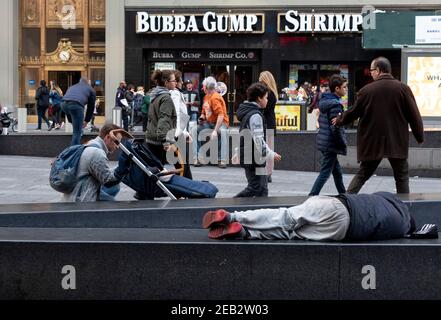 Un homme dort dans Times Square tandis que les touristes marchent. Banque D'Images