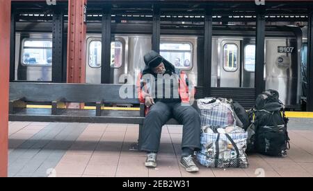 Un homme sans abri apparent dort dans le métro de la ville de New York avec ses possessions. Banque D'Images