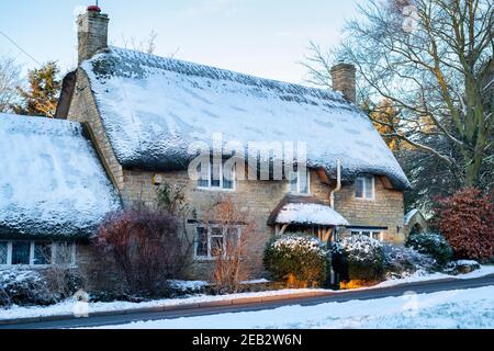 Chalet de chaume dans la neige de janvier au lever du soleil. Long Compton, Warwickshire, Angleterre Banque D'Images