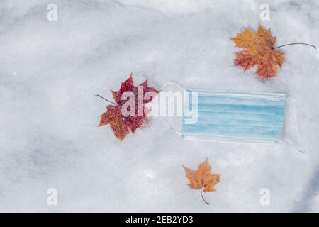 Masque médical et feuille d'érable jaune sur la neige. Concept de santé, protégez-vous pendant les vacances d'hiver. Photo de haute qualité Banque D'Images