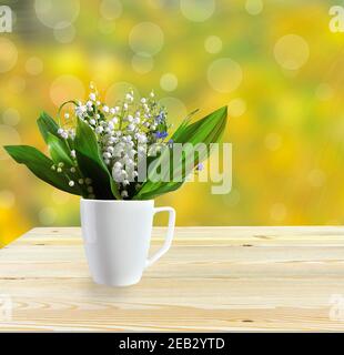 Printemps ou été encore la vie avec des lilas délicats de la vallée et des fleurs oubliées-me-pas dans la tasse blanche sur table en bois. Bouquet de nénuphars de la vallée f Banque D'Images