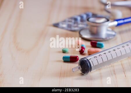 Fermez la seringue, le stéthoscope bleu et les comprimés avec des comprimés sur une table en bois. Concept de santé et de médecine Banque D'Images