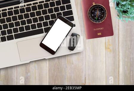 Bureau table avec matériel de bureau, ordinateur portable, smartphone, clé de voiture, passeport, boussole et fleur sur fond de table en bois. Vue de dessus avec co Banque D'Images