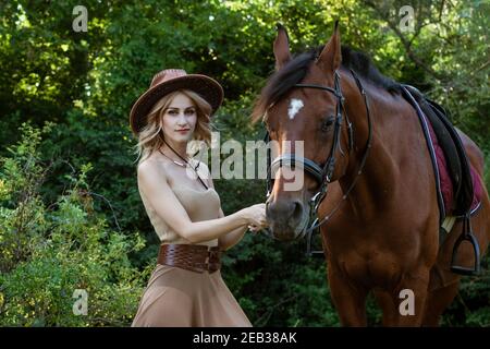 Belle jeune femme dans un chapeau de cow-boy près d'un cheval sur la nature dans le parc Banque D'Images