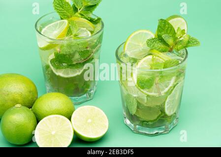 Des cocktails Mojito rafraîchissants dans les verres avec des tranches fraîches limes et feuilles de menthe poivrée sur fond vert Banque D'Images