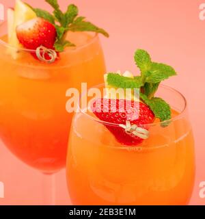 Gros plan sur les boissons rafraîchissantes aux fraises et à l'orange au lever du soleil dans les verres sur fond rose corail Banque D'Images