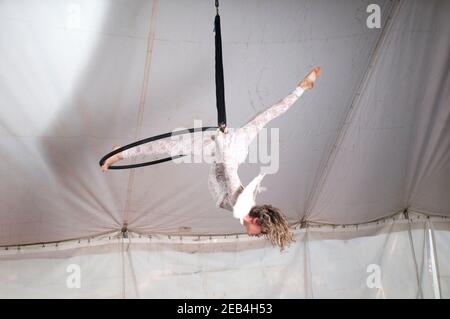 La femme Aerialist acrobat avec des ailes d'angle se produit dans l'air sur un cerceau dans une tente de cirque Banque D'Images