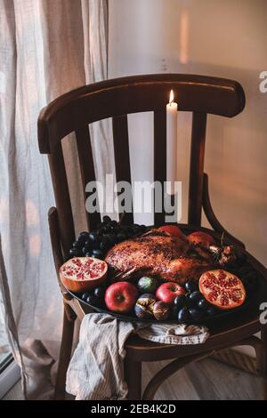 Canard rôti au four entier avec fruits de saison et bougie pour les vacances de Thanksgiving ou la fête de Noël sur plateau sur chaise en bois, vue sur le dessus. Repas de confort traditionnel pour les vacances d'automne ou d'hiver Banque D'Images