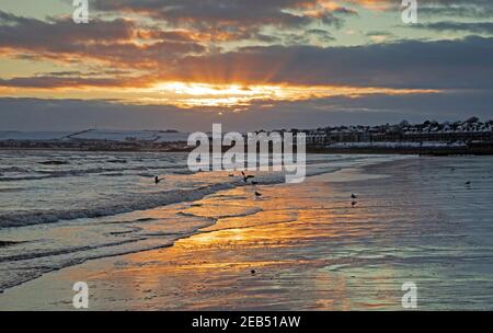 Portobello, Édimbourg, Écosse, Royaume-Uni. 12 février 2021, Sunrise sunbeam à Firth of Forth, avec une température de moins 1 degré. En photo : un faisceau de soleil, en optique météorologique, est un faisceau de lumière du soleil qui semble rayonner de la position du Soleil. Brillant par des ouvertures dans les nuages ou entre d'autres objets tels que des montagnes et des bâtiments, ces faisceaux de lumière du soleil diffuse des particules sont séparés par des volumes sombres. Banque D'Images