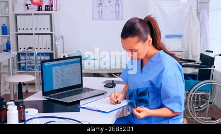 Le personnel infirmier vérifie le résultat des rayons X, lit la liste des patients, prend des notes dans le presse-papiers en tenant la radiographie. Médecin en médecine uniforme rédaction de la liste des patients consultés, diagnostiqués, faisant de la recherche. Banque D'Images