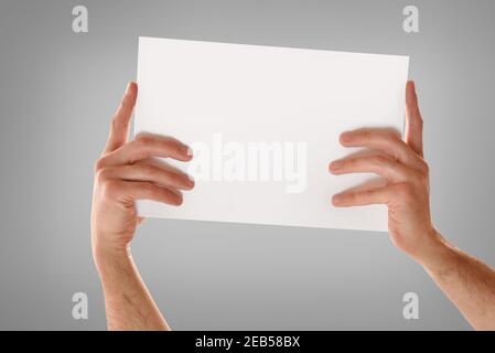 Deux mains attrapent la feuille blanche horizontalement avec les doigts étirés sur le bord avec un arrière-plan dégradé de gris isolé Banque D'Images