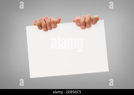 Deux mains tenant la feuille de papier blanche horizontalement par le haut avec un arrière-plan dégradé de gris isolé Banque D'Images