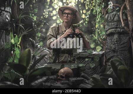 Femme courageuse explorant la jungle tropicale et trouvant des ruines antiques, elle tient des jumelles et regarde autour Banque D'Images
