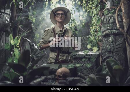 Femme courageuse explorant la jungle tropicale et trouvant des ruines antiques, elle tient des jumelles et regarde autour Banque D'Images