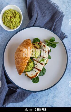 Sandwich croissant avec fromage halloumi grillé, arugula et courgettes grillées, fond en béton bleu. Petit déjeuner ou déjeuner sain. Mise au point sélective. Banque D'Images