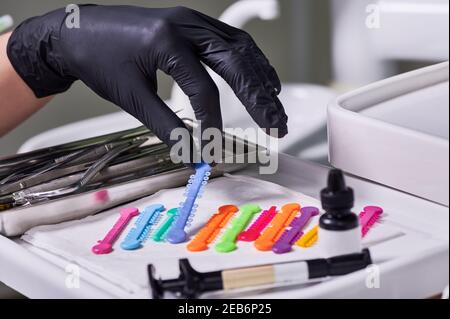 Gros plan de la main du médecin dans un gant stérile saisissant une cravate de ligature orthodontique bleue. Dentiste prenant un élastique ou un joint torique orthodontique pour les bretelles. Concept de la dentisterie et de l'orthodontie. Banque D'Images