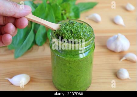 Main tenant une cuillère en bois ramasse de sauce de pesto de basilic frais ou Pesto Alla Genovese de la bouteille Banque D'Images