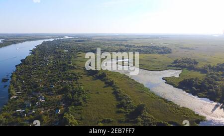 Un drone survole une rivière de couleur bleue entourée de tournieaux Village local avec divers bâtiments et habitat des marais et des marais Avec une nouvelle édition de Common Re Banque D'Images