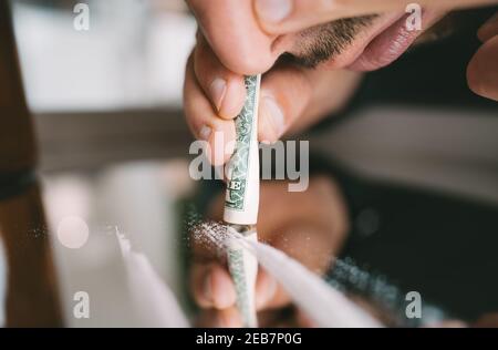 Junkie homme renifler ou ronfler des lignes de cocaïne sur le miroir à travers le billet de banque roulé. Style de vie préjudiciable. Mauvaises habitudes Banque D'Images