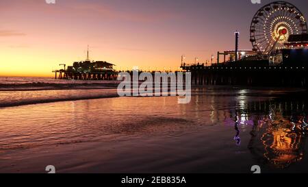 Des vagues de crépuscule contre une grande roue lumineuse classique, parc d'attractions sur la jetée de Santa Monica pacific Ocean Beach Resort. Symbole emblématique de l'été o Banque D'Images