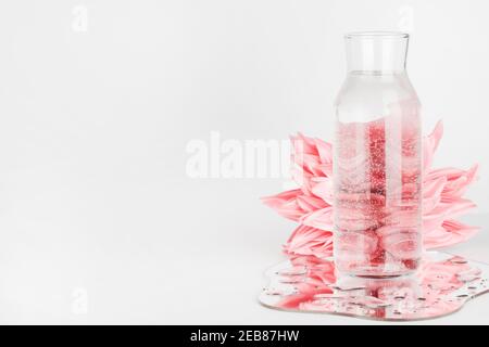 fleurs roses déformées par l'eau en bouteille avec miroir sur fond blanc. eau pure, détente, surréaliste, concept de maison écologique. espace copie. Banque D'Images