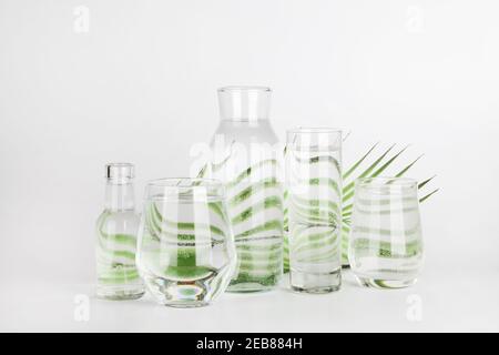 feuille de palmier déformée par l'eau dans les verres et les bouteilles sur fond blanc. Décoration d'intérieur, écologique, eau pure, concept de jardinage.nature fond Banque D'Images