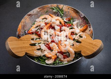 Salade d'arugula ou de roquette aux crevettes ou crevettes, tomates, champignons de Paris, servis dans un grand bol avec des serveurs en bois Banque D'Images