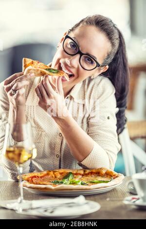 Une jeune femme mignonne s'incline la tête tandis qu'elle s'incline dans une tranche de pizza. Banque D'Images