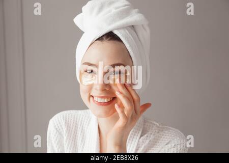 Jolie fille européenne appliquant des patchs de collagène doré sous ses yeux. Femme traitement du visage. Cosmétologie, beauté et spa Banque D'Images