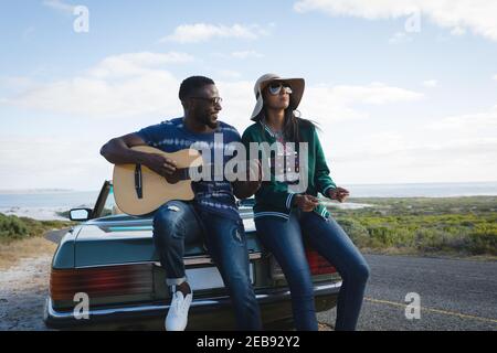 Divers couples prenant une pause au bord de la route le jour ensoleillé à côté du cabriolet voiture l'homme jouant de la guitare Banque D'Images